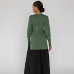 Person wearing a green long-sleeve top and black wide-leg pants on a white background