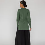 Person wearing a green long-sleeve top and black wide-leg pants on a white background