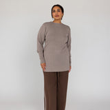 Woman wearing a beige long-sleeve top and brown wide-leg pants on a white background