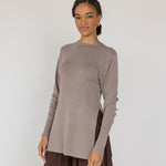Woman wearing a brown long-sleeve top and brown skirt against a white background