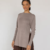 Woman wearing a brown long-sleeve top and brown skirt against a white background