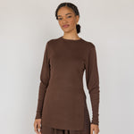 Woman wearing a brown long-sleeve top and wide-leg pants against a white background