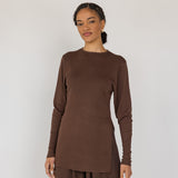 Woman wearing a brown long-sleeve top and wide-leg pants against a white background