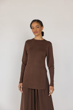 Woman wearing a brown long-sleeve top and wide-leg pants against a white background