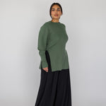 Woman wearing a green knit top and black pants on a white background