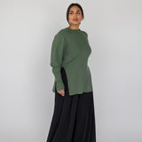 Woman wearing a green knit top and black pants on a white background