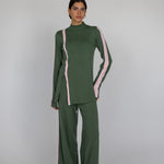 Model styled in a green top and pants with pink accents on a white background