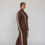 Woman wearing a brown matching set with truffle stripes on a plain background