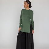 Woman wearing a green long-sleeve top and black wide-leg pants on a white background
