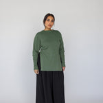 Woman wearing a green long-sleeve top and black wide-leg pants on a white background