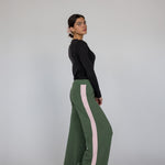 Woman wearing green pants with pink stripes and a black top on a gray background