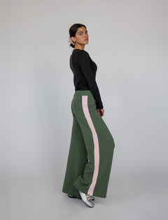 Woman wearing green pants with pink stripes and a black top on a gray background