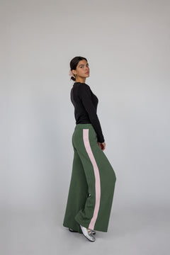 Woman wearing green pants with pink stripes and a black top on a gray background