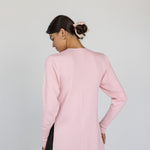 Woman wearing a light pink top over a black outfit on a plain background