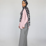 Woman wearing a patterned leopard hijab, pink top, gray pants, and white shoes on a white background