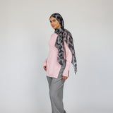 Woman wearing a pink top, gray pants, and a patterned leopard hijab on a white background