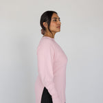 Woman wearing a pink sweater and black pants against a white background