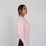Woman wearing a pink sweater and black pants against a white background
