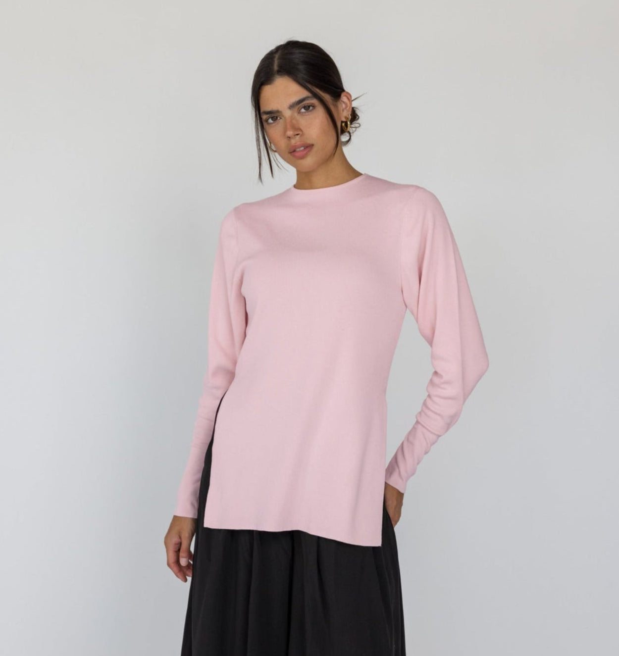 Woman wearing a light pink long-sleeve top and black pants on a white background