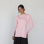 Woman wearing a light pink long-sleeve top and black pants on a white background