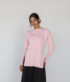 Woman wearing a light pink long-sleeve top and black pants on a white background