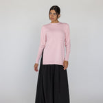 Person wearing a light pink knit top and black skirt on a white background
