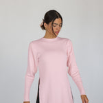 Woman wearing a light pink knit top with slits against a gray background