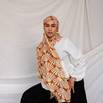 Woman wearing a Amber Shells printed hijab, white shirt, and black pants against a plain background.