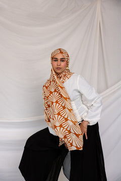 Woman wearing a Amber Shells printed hijab, white shirt, and black pants against a plain background.