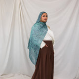 A model posing in the Aqua Cobra scarf, a teal and blue snakeskin print scarf. Model is also wearing the VELA Palazzo pant. 