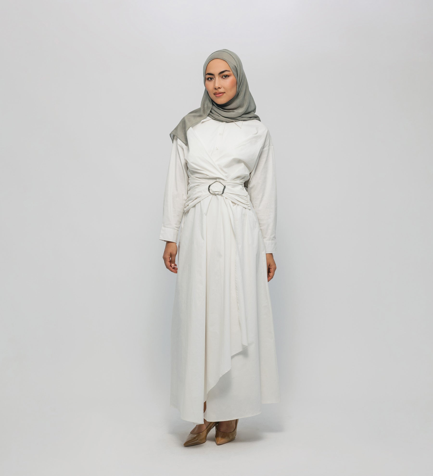 Woman wearing a white dress with a belt and a gray hijab on a white background