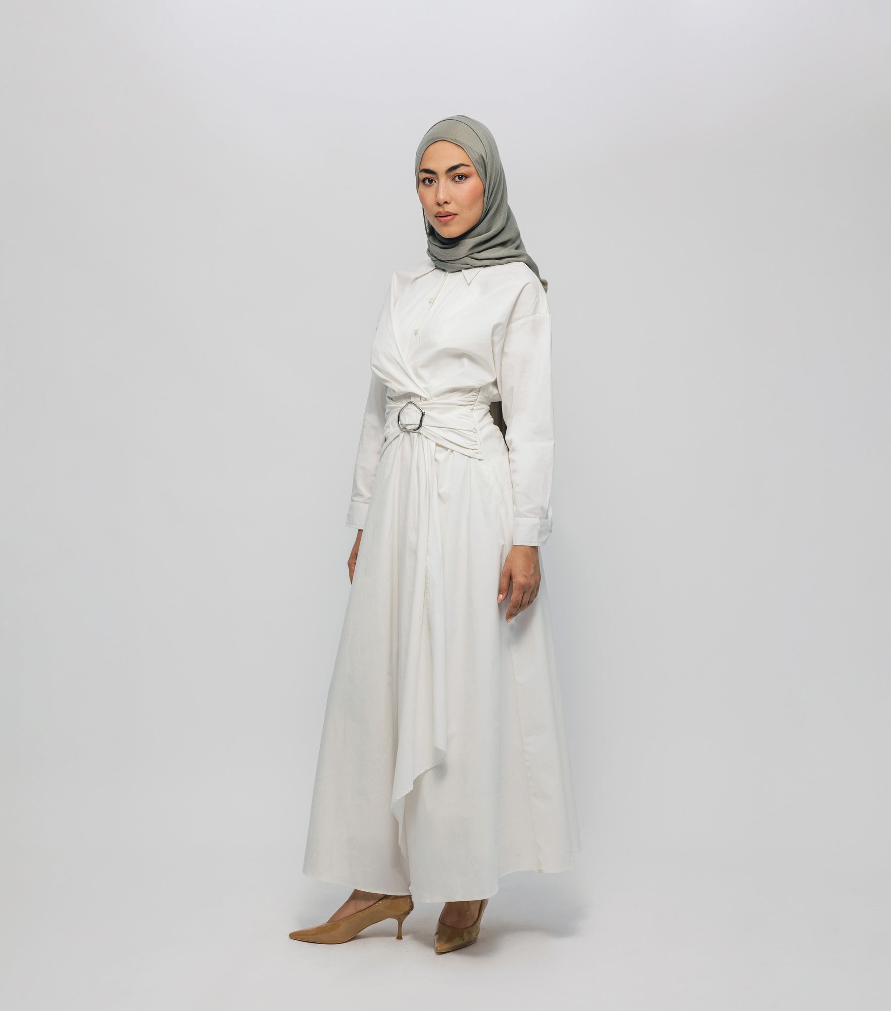Woman wearing a white outfit with a belt and a gray hijab on a white background