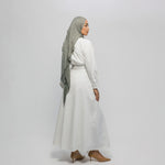 Woman wearing a white outfit with a gray hijab on a plain background