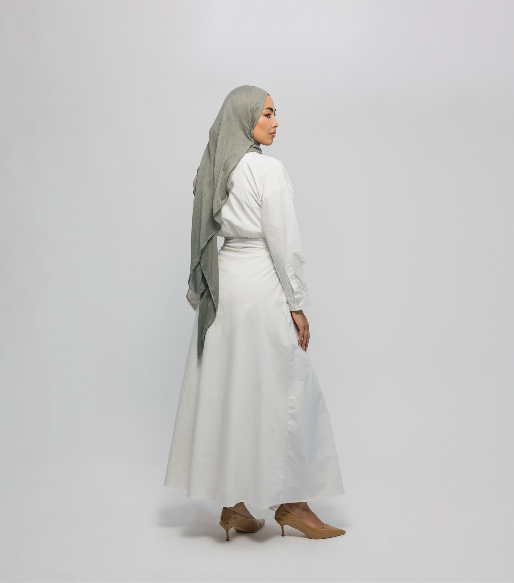 Woman wearing a white outfit with a gray hijab on a plain background