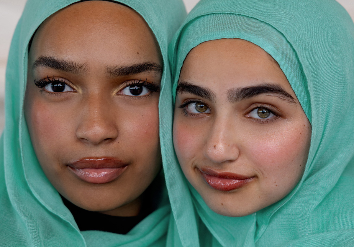 Two young women wearing matching mint green hijabs, shown in a close-up portrait against a soft light background.