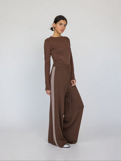 Woman wearing a brown long-sleeve top and wide-leg pants with a white background
