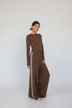 Woman wearing a brown long-sleeve top and wide-leg pants with a white background