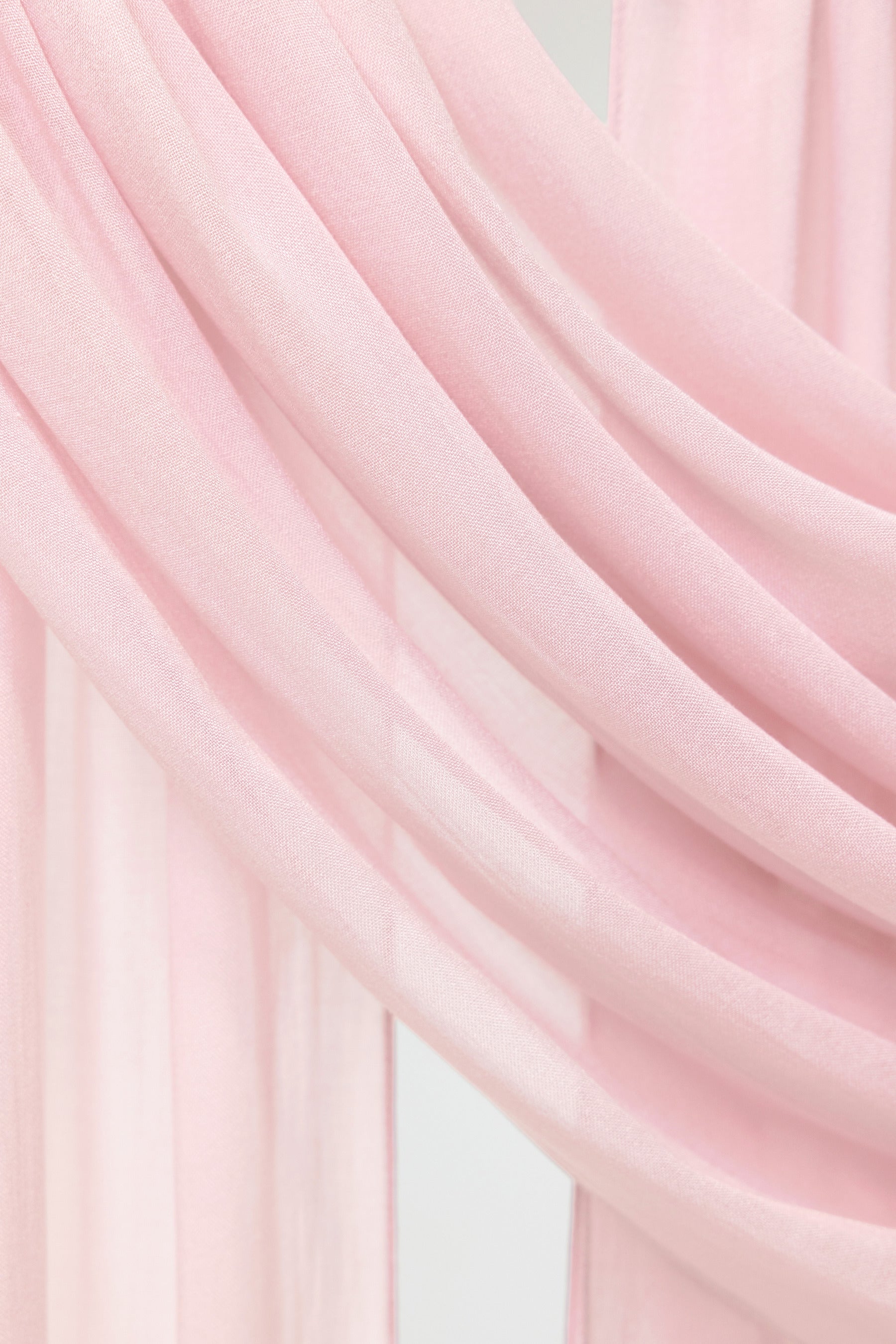 A close-up of draped light pink fabric, showing soft folds and a smooth texture.