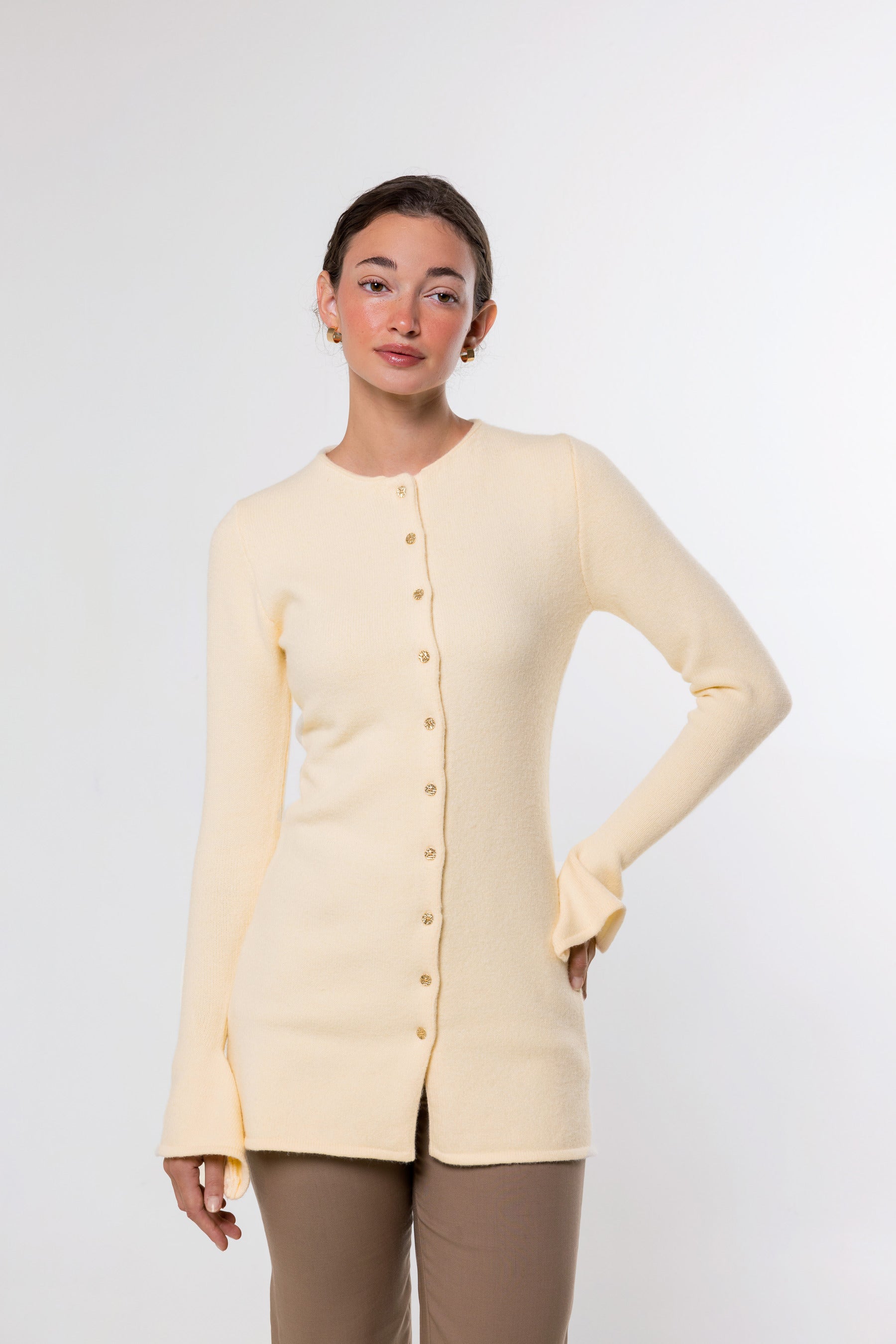 A woman modeling a pale cream long-sleeve knit cardigan with a button front, photographed against a clean light gray studio background.
