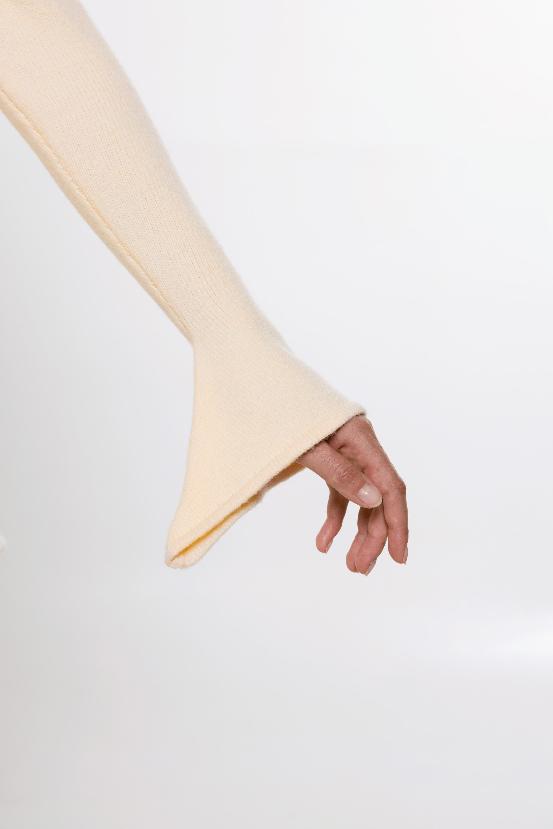 A close-up of a hand wearing a cream-colored ribbed knit sleeve with a flared cuff, set against a plain white background.