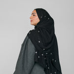 Woman wearing a black hijab with star beaded patterns on a gray background