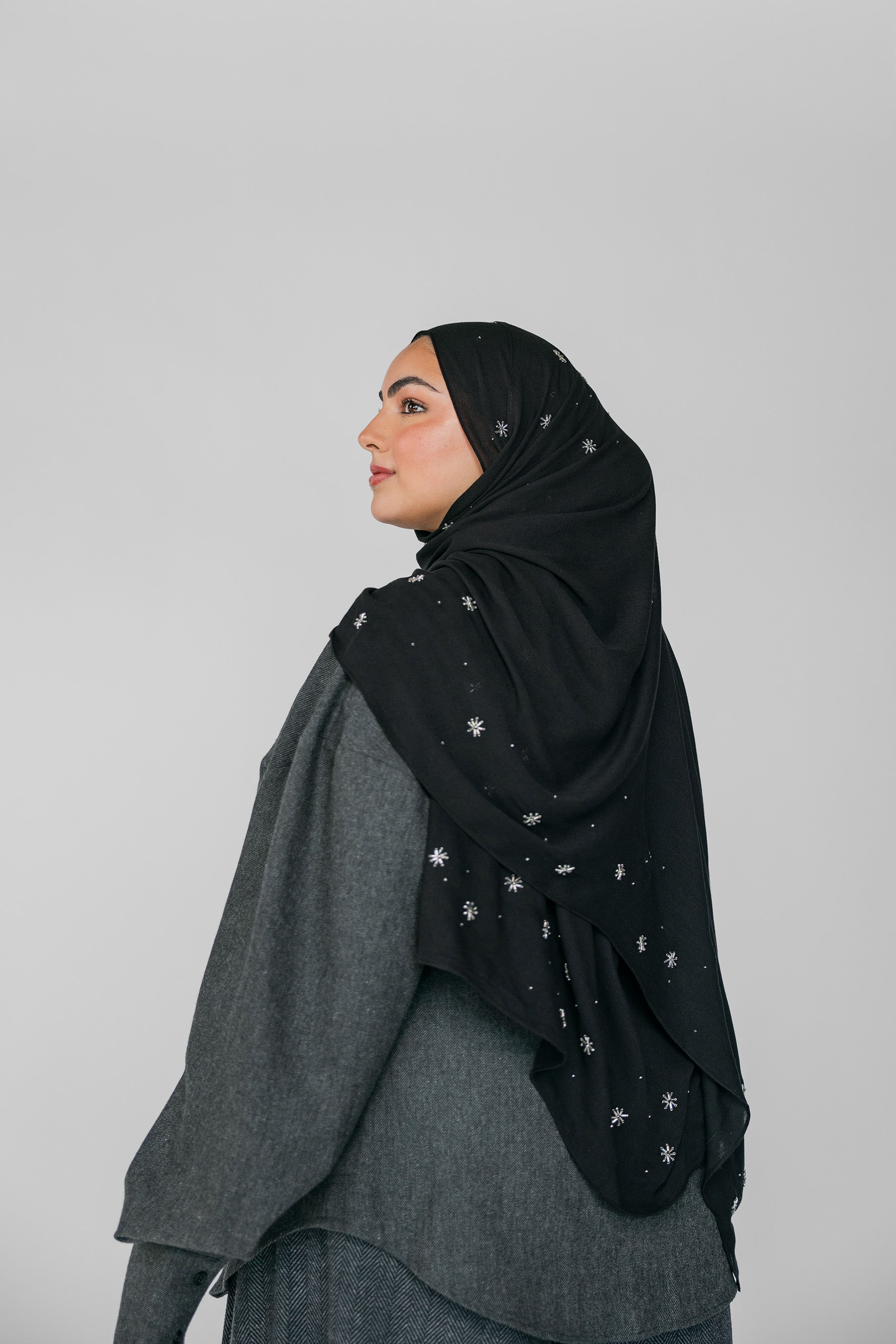 Woman wearing a black hijab with star beaded patterns on a gray background