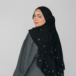 Woman wearing a black hijab with white beadeed patterns on a gray background
