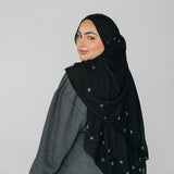 Woman wearing a black hijab with white beadeed patterns on a gray background