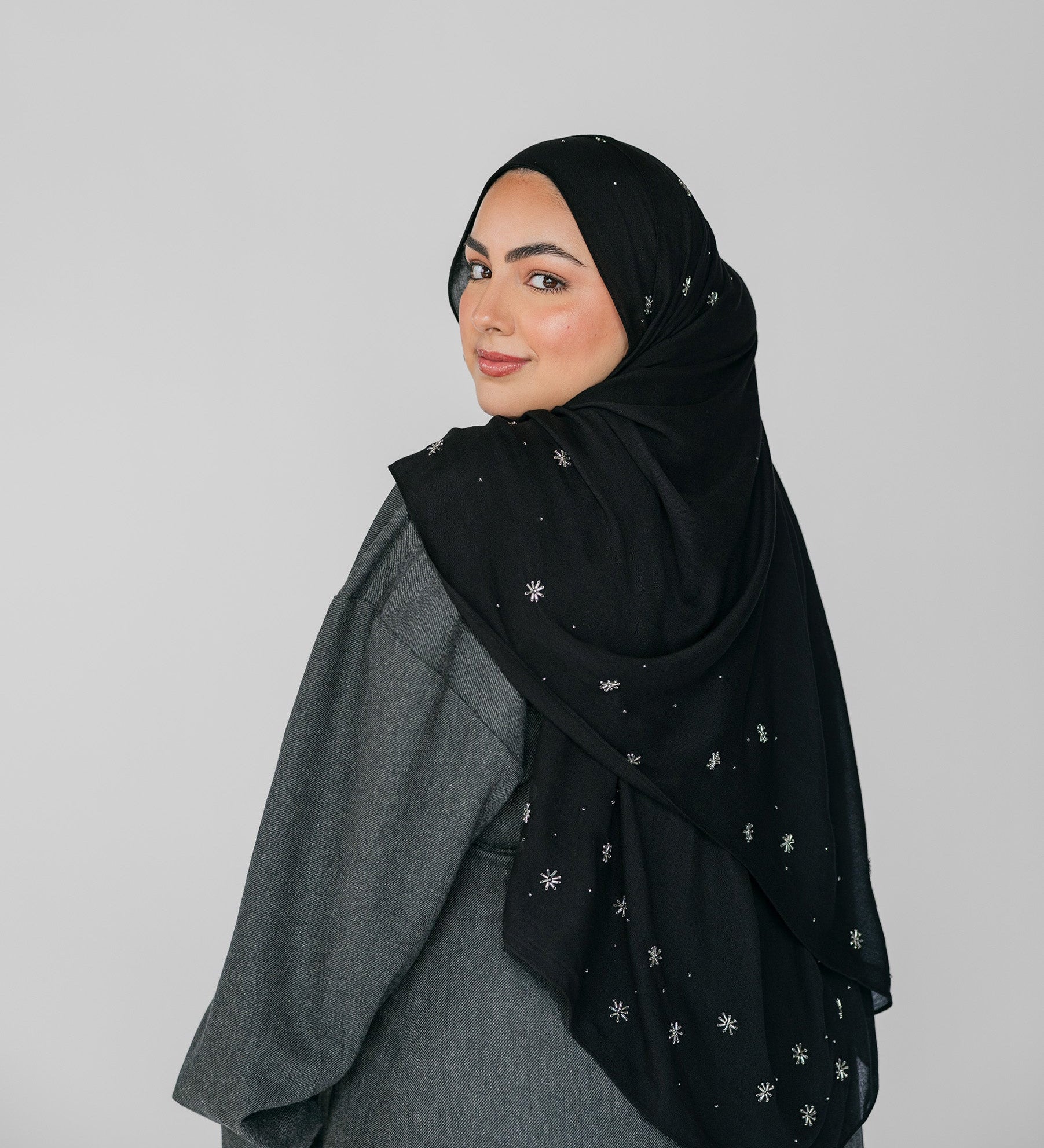 Woman wearing a black hijab with white beadeed patterns on a gray background