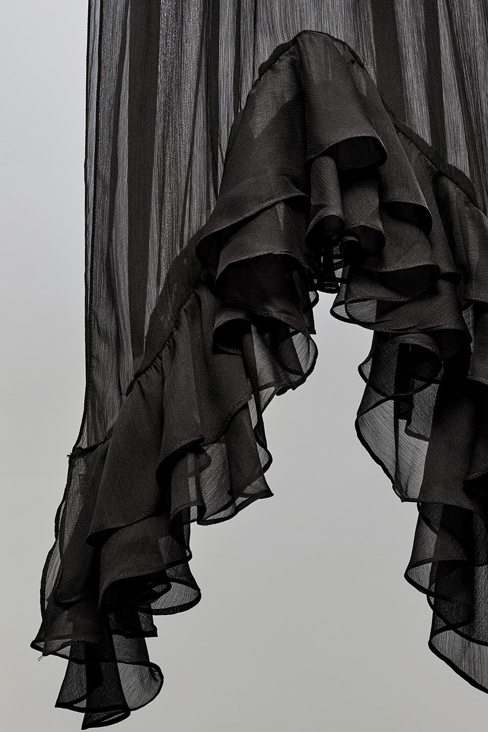 Black sheer ruffled fabric, likely a curtain or scarf, hanging against a plain light gray background.