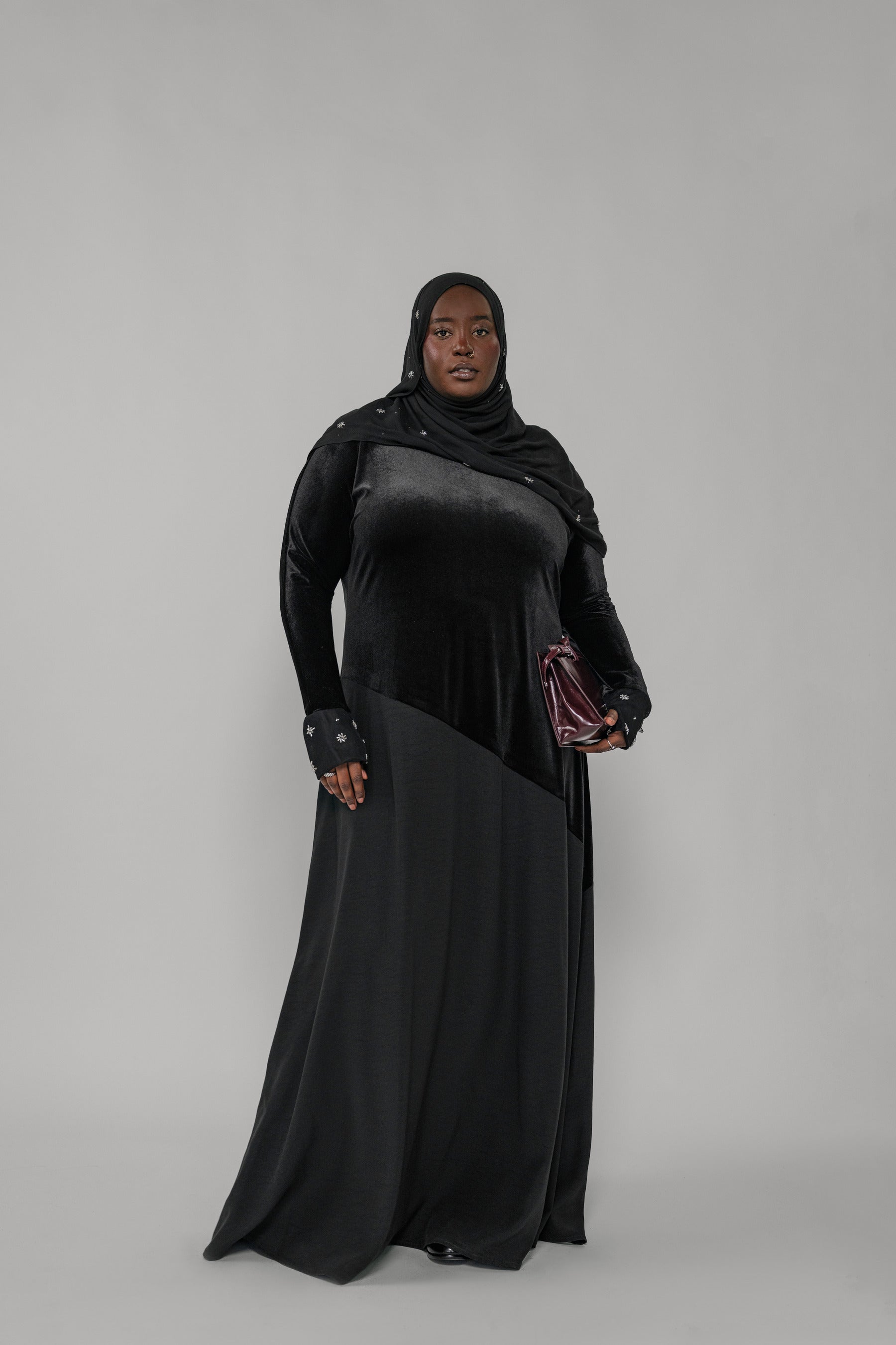 Woman wearing a black abaya and hijab on a gray background