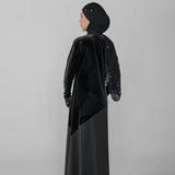 Woman wearing a black abaya and hijab on a gray background
