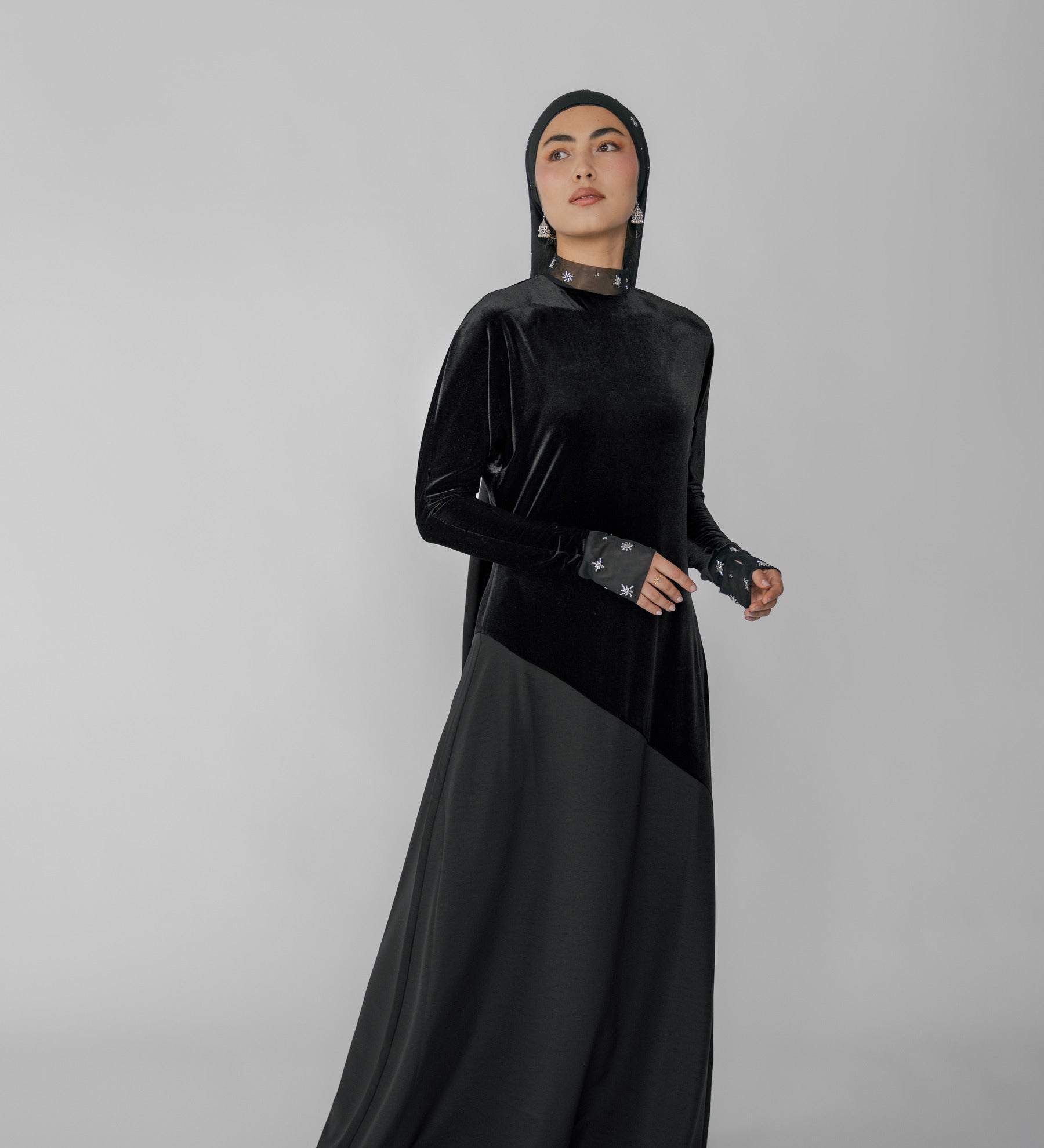 Woman wearing a black abaya with a hijab on a gray background