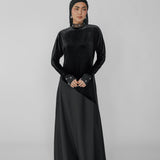 Woman wearing a black dress with a hijab on a gray background
